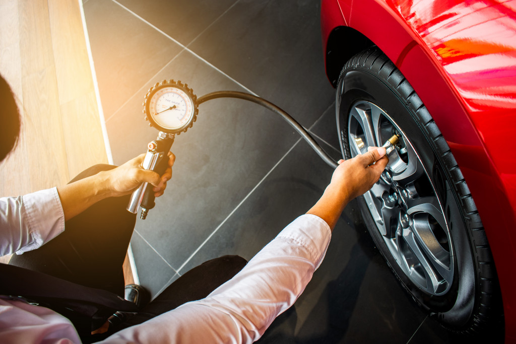 businessman holding pressure gauge and checking tire pressure of a red car