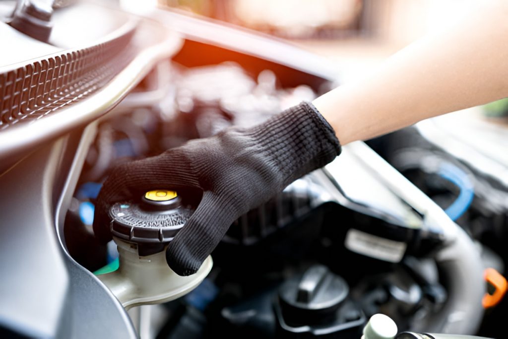 close-up of a gloved hand opening a car's brake fluid reservoir cap