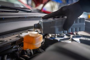 person wearing black gloves refilling brake fluid
