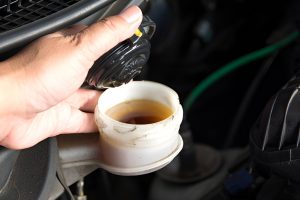 person holding the cap of a car's brake fluid reservoir