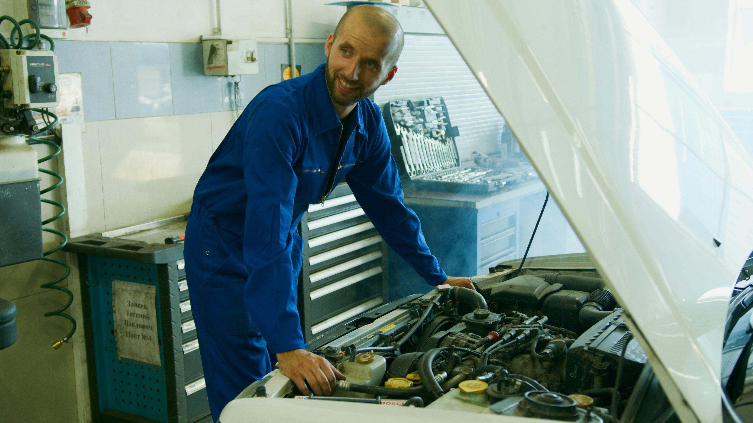 smiling mechanic standing under a car's open hood
